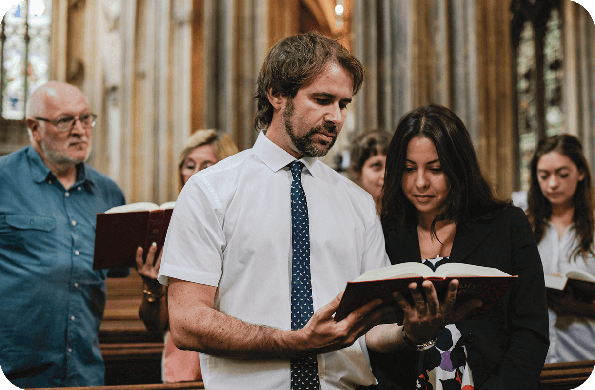 A group of people standing in a church, hymn books in hand, unite their voices as they sing or recite together, each one experiencing personal faith journeys.