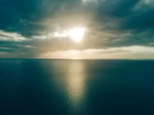 Sunlight piercing through dramatic clouds over a calm sea.