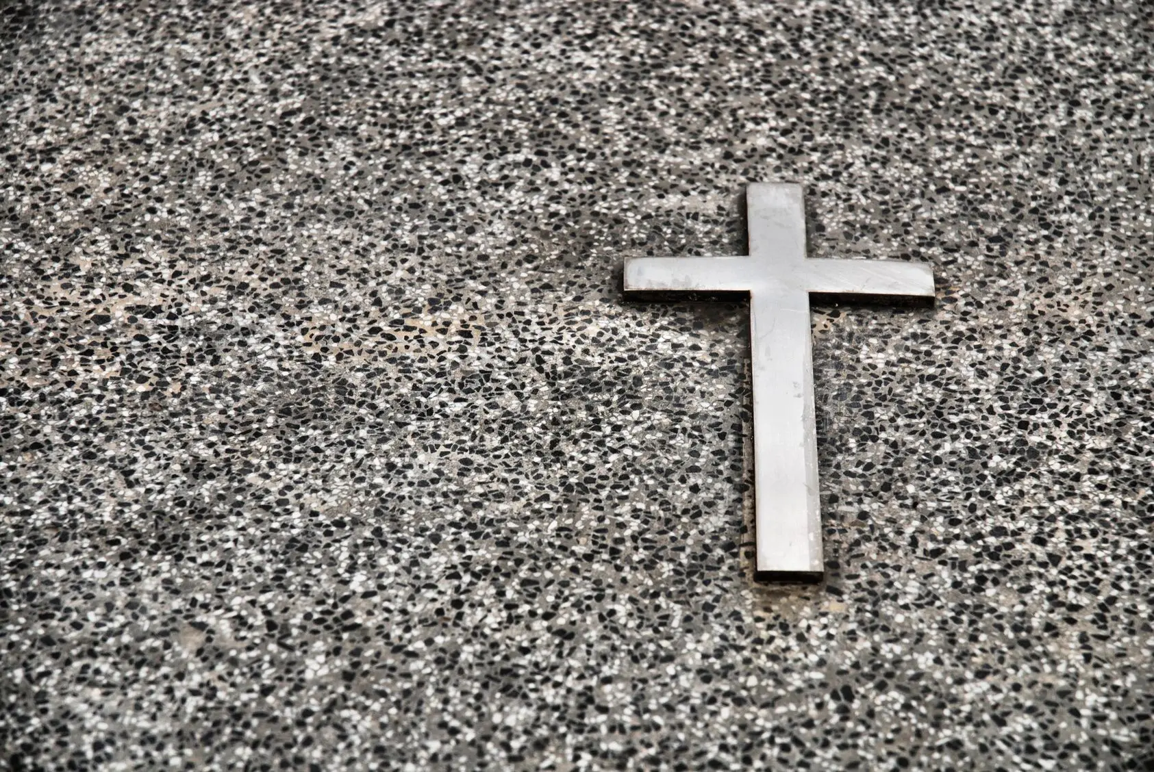 A silver cross on a speckled granite surface.