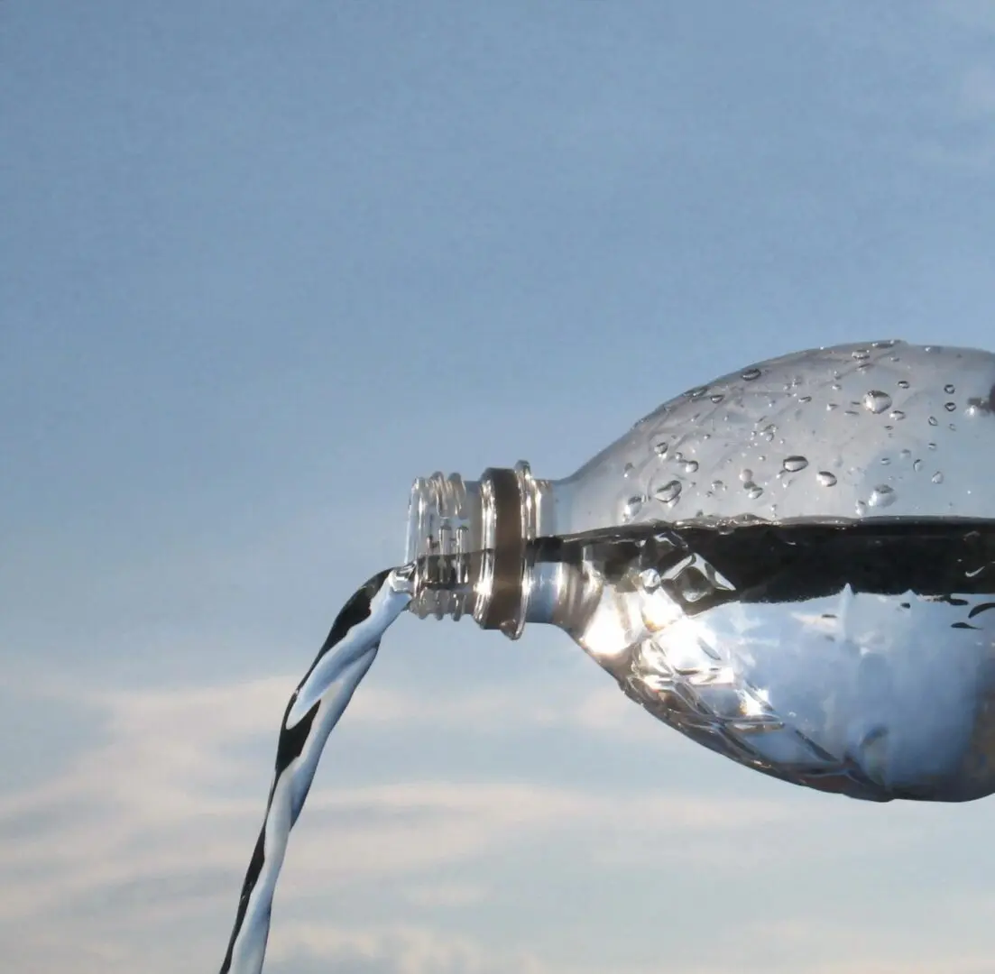 Water pouring from a plastic bottle against a sky background.