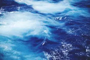 Swirling blue ocean waves with white foam under sunlight.