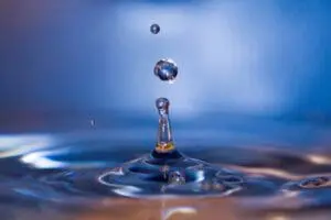Close-up of water droplets creating ripples on a blue surface.