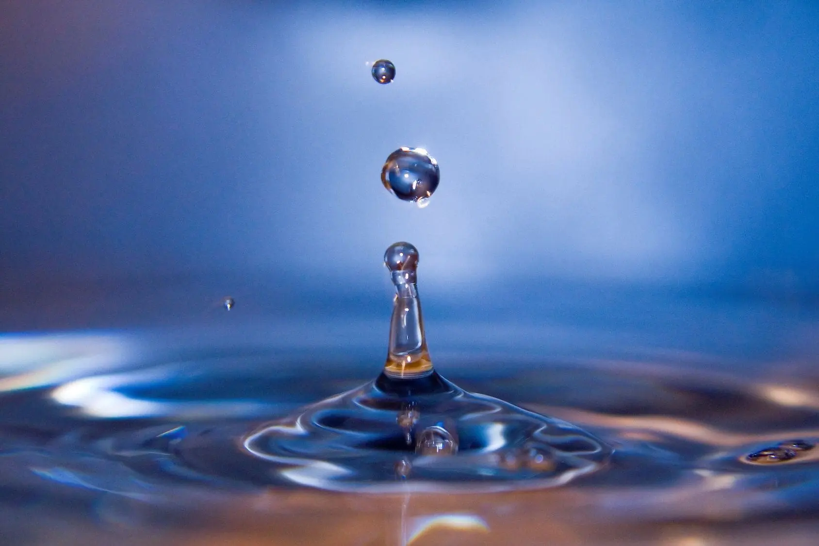 Close-up of water droplets creating ripples on a blue surface.