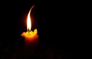 A single glowing candle flame against a dark background.