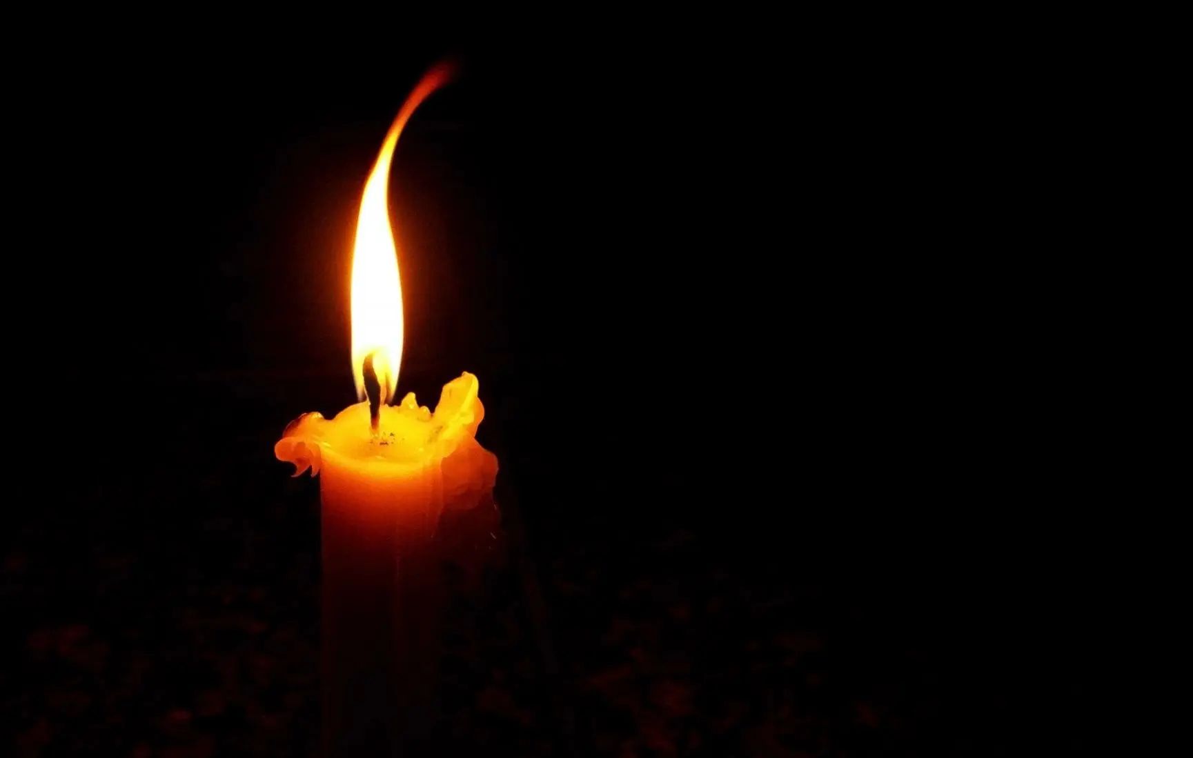 A single glowing candle flame against a dark background.