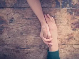 Two people holding hands over a wooden surface, symbolizing support.