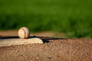 A baseball resting on home plate on a dirt field with green grass in the background.