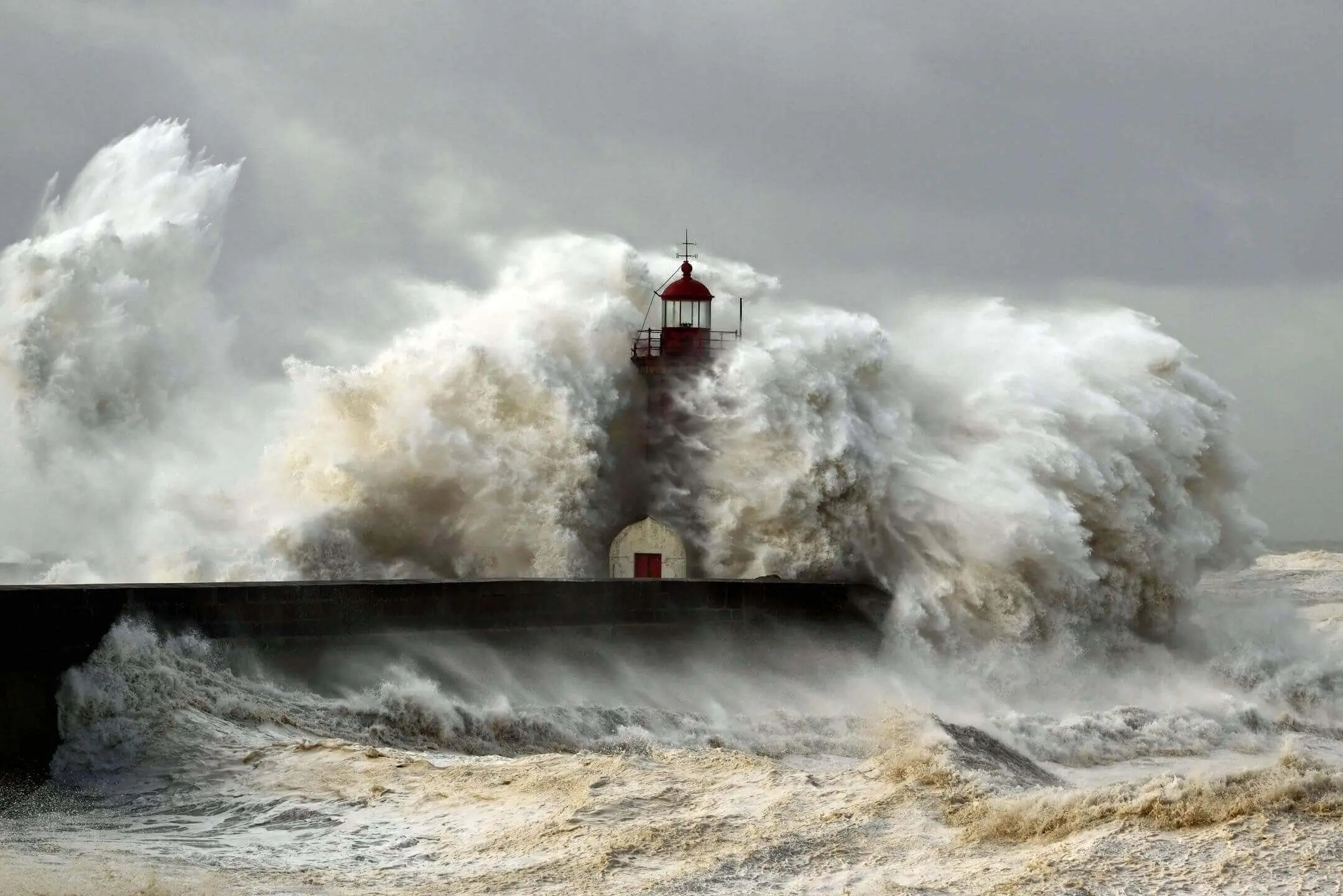 Powerful waves crash against a lighthouse on a stormy sea.