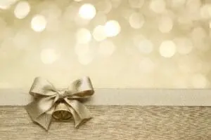 Elegant gold gift box with a bow on a wooden surface and bokeh lights.
