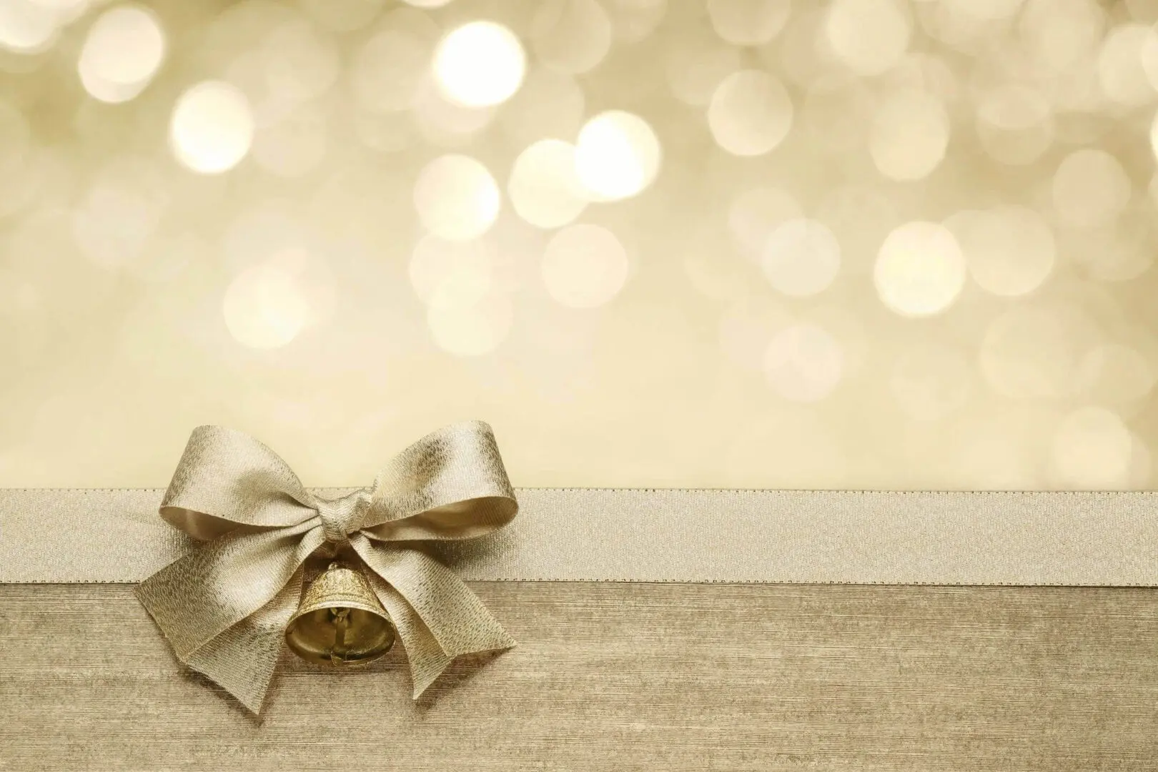 Elegant gold gift box with a bow on a wooden surface and bokeh lights.