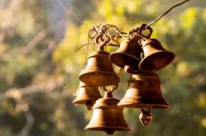 Rustic metal bells hanging outdoors with blurred natural background.