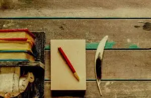 A notepad with a red pen and a feather on a wooden surface.