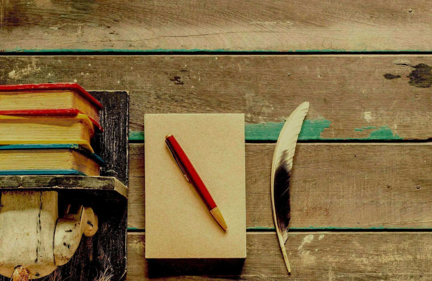A notepad with a red pen and a feather on a wooden surface.