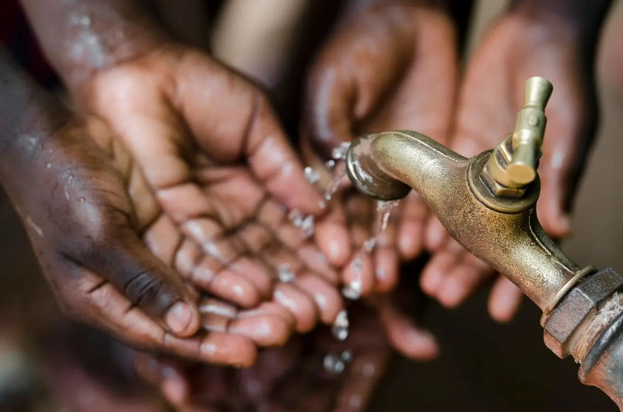 Hands catching water poured from a traditional vessel.