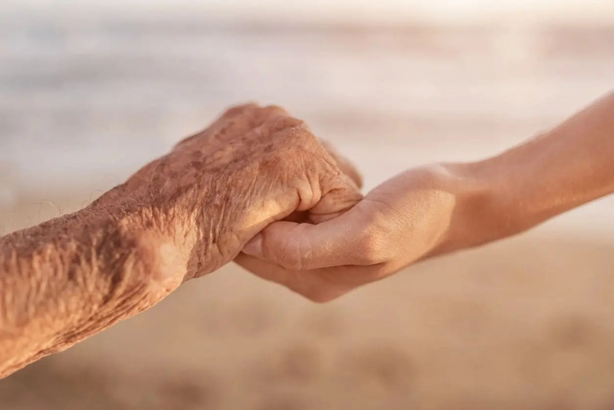 An elderly hand holding a younger hand symbolizing care and connection.