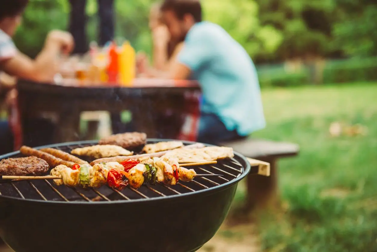 Skewers grilling on a barbecue with a person blurred in the background.