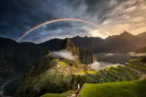 A vibrant rainbow arches over the ancient ruins of Machu Picchu at sunset.