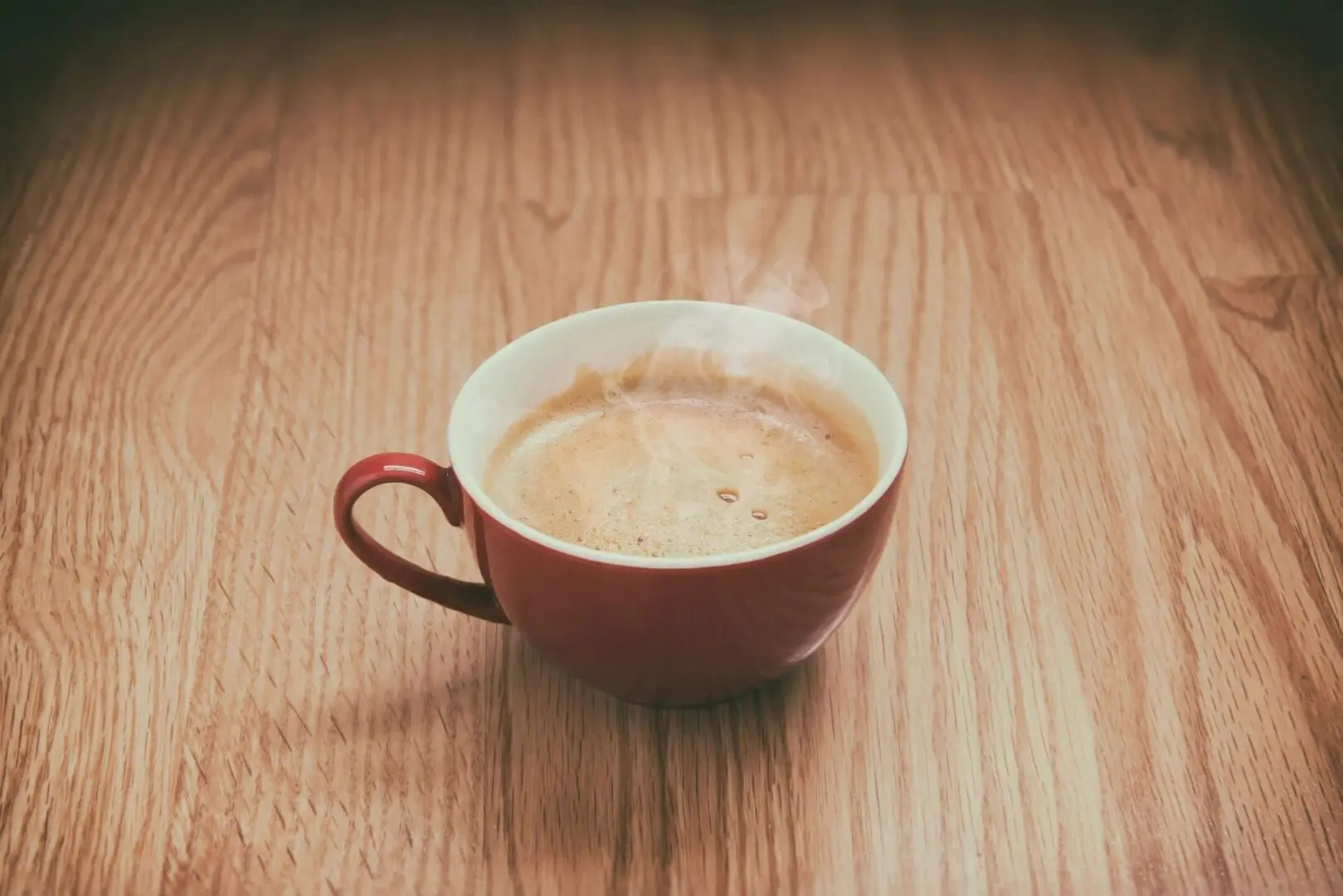 A cup of coffee with frothy foam on a wooden table.