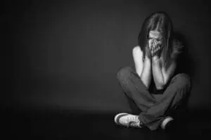 A young woman sitting on the floor, covering her face, appearing distressed.