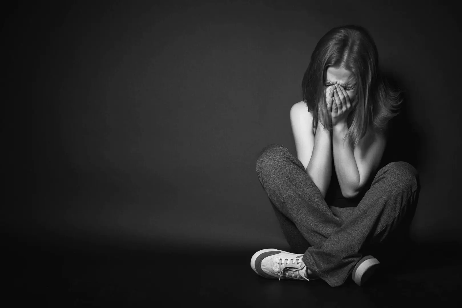A young woman sitting on the floor, covering her face, appearing distressed.