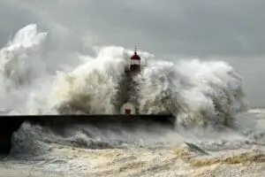 Waves crash powerfully against a lighthouse in stormy weather.