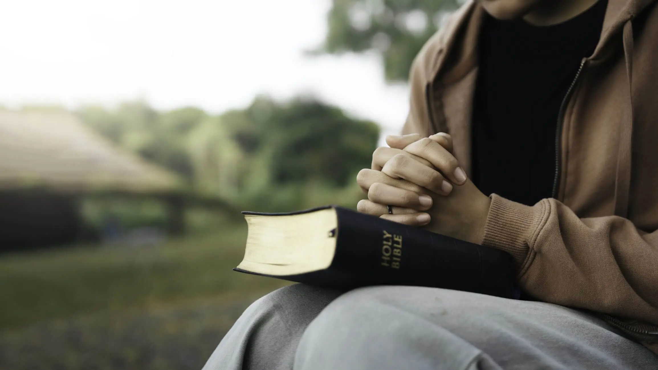 Person holding a Bible with hands clasped in prayer.