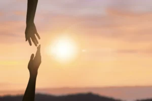 Two hands reaching out towards each other at sunset.