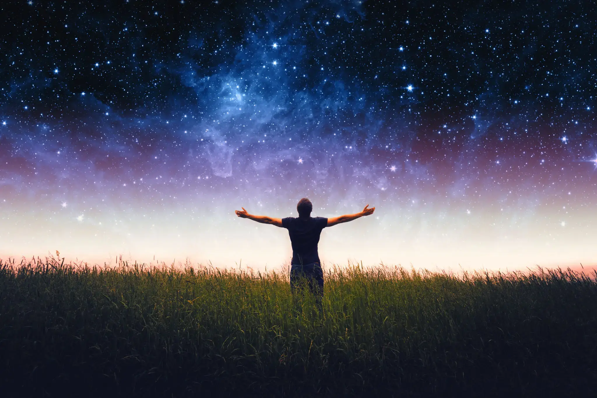 Person standing with arms open under a starry night sky.