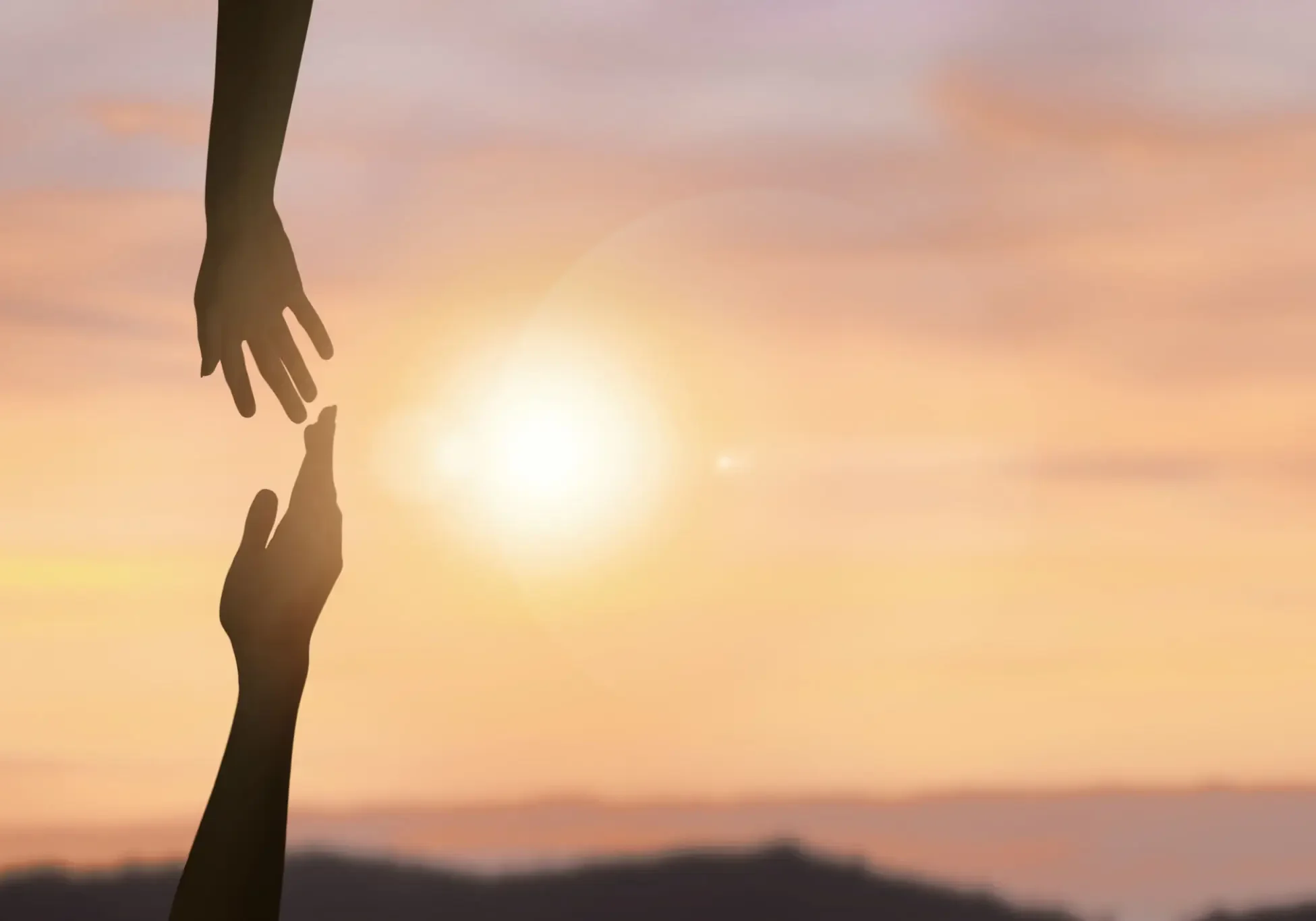 Two hands reaching out towards each other at sunset.