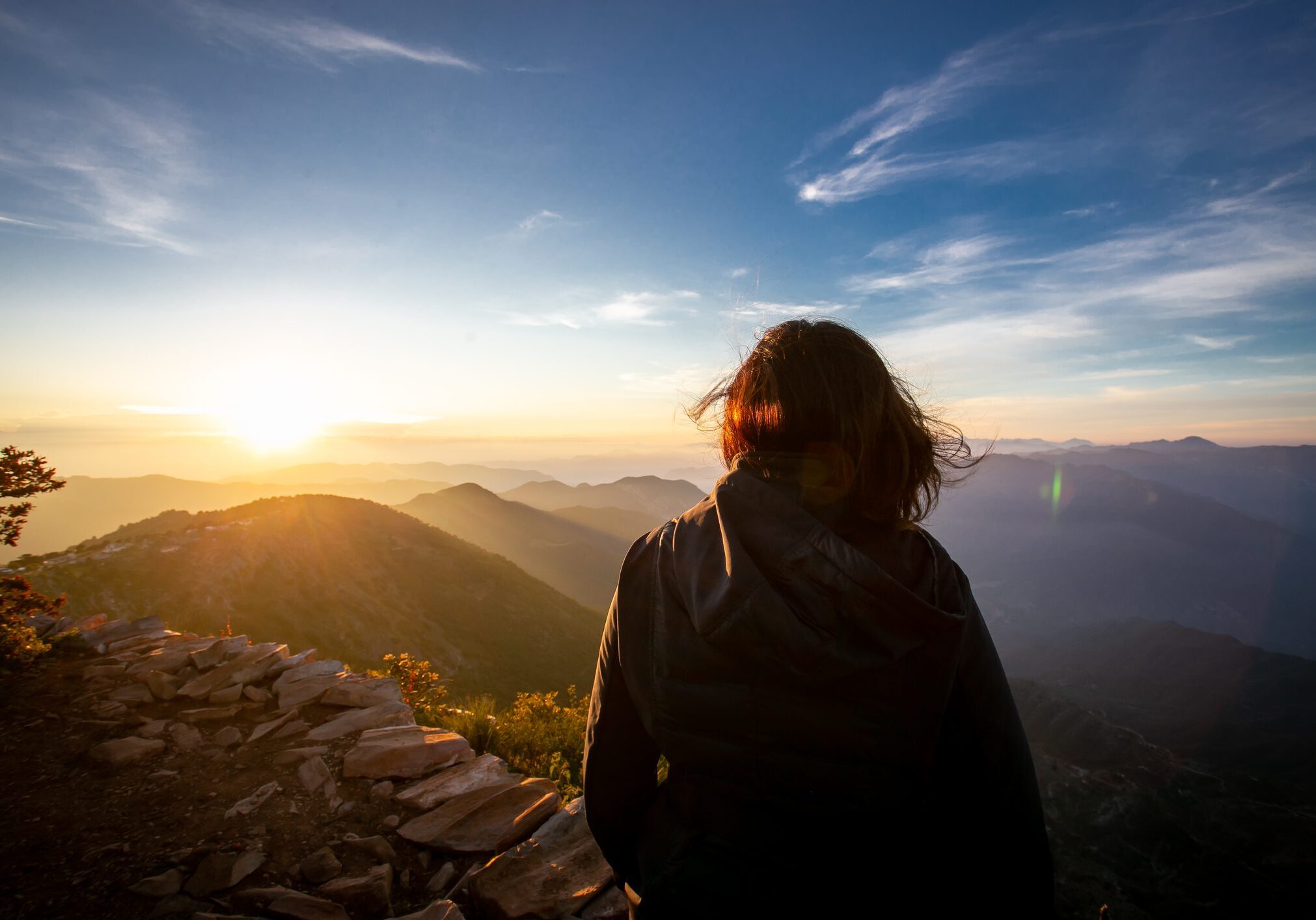 Person watching sunset over mountains from a rocky viewpoint.