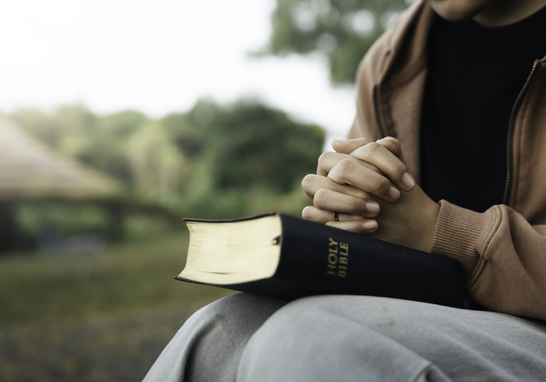 Person holding a Bible with hands clasped in prayer.
