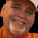 Smiling man with white beard and cap.