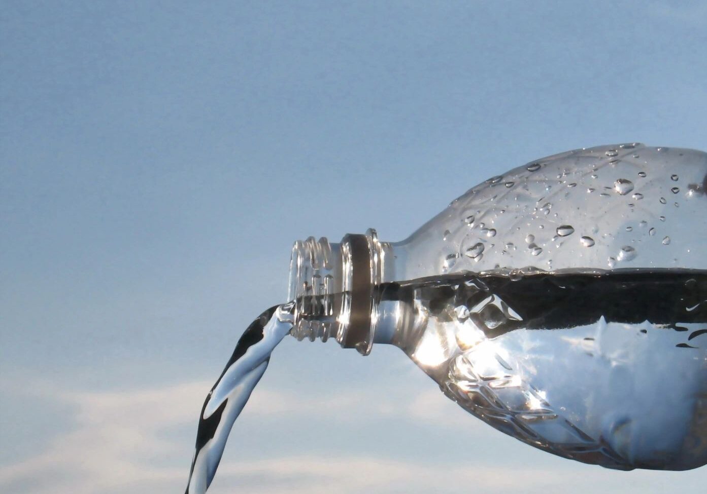 Water pouring from a plastic bottle against a sky background.