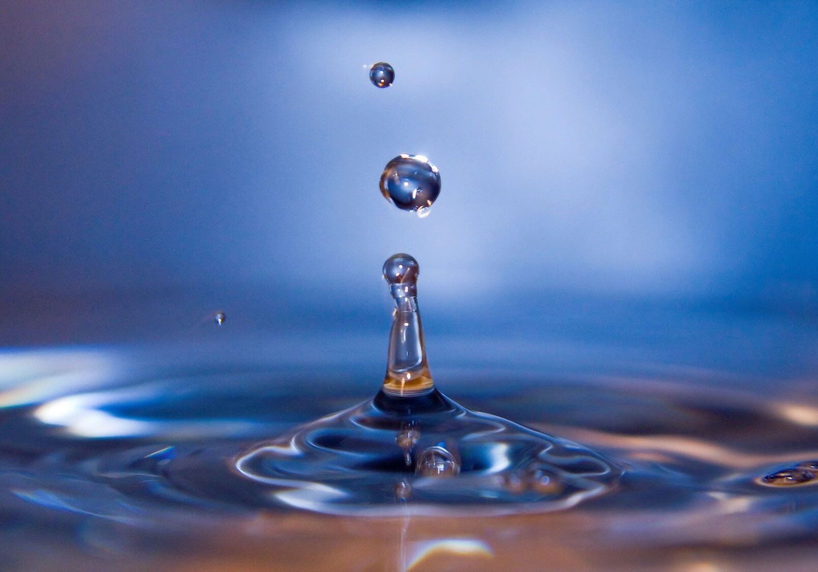 Close-up of water droplets creating ripples on a blue surface.