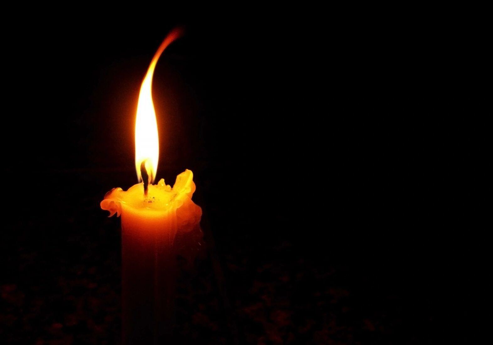 A single glowing candle flame against a dark background.
