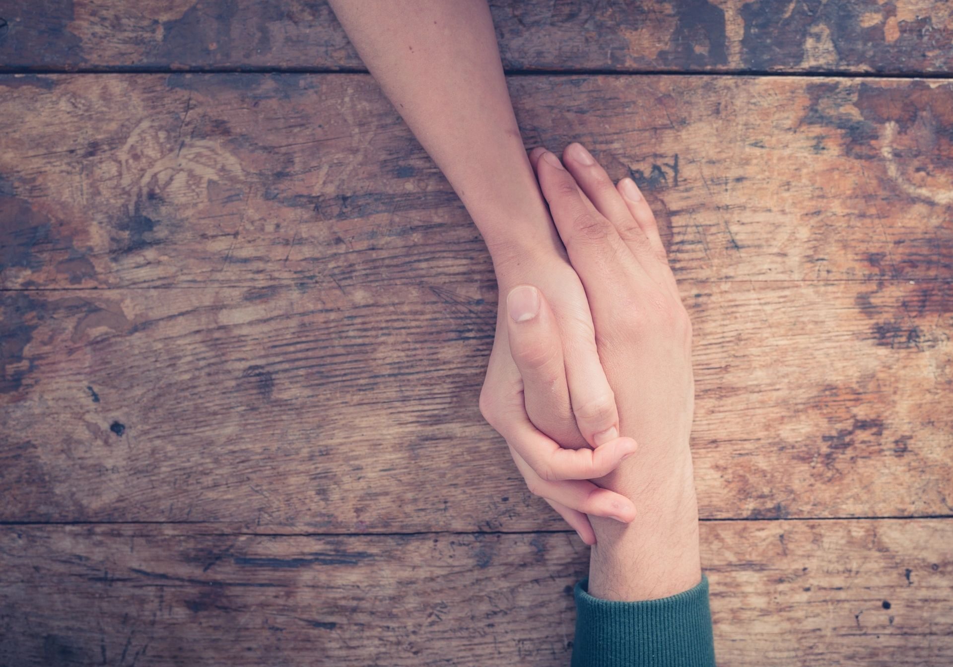 Two people holding hands over a wooden surface, symbolizing support.