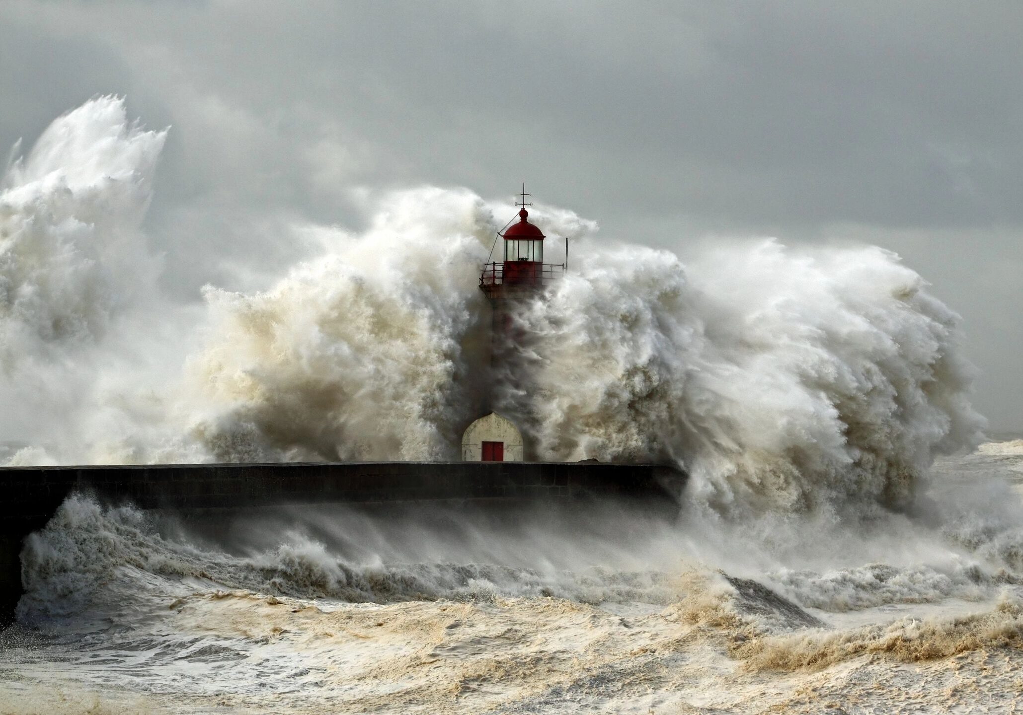 Powerful waves crash against a lighthouse on a stormy sea.
