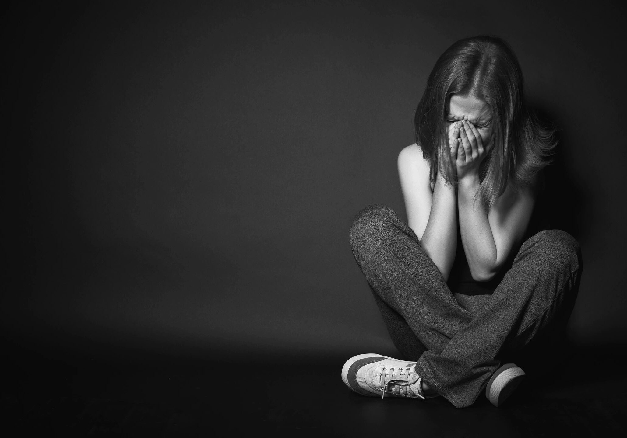 A young woman sitting on the floor, covering her face, appearing distressed.