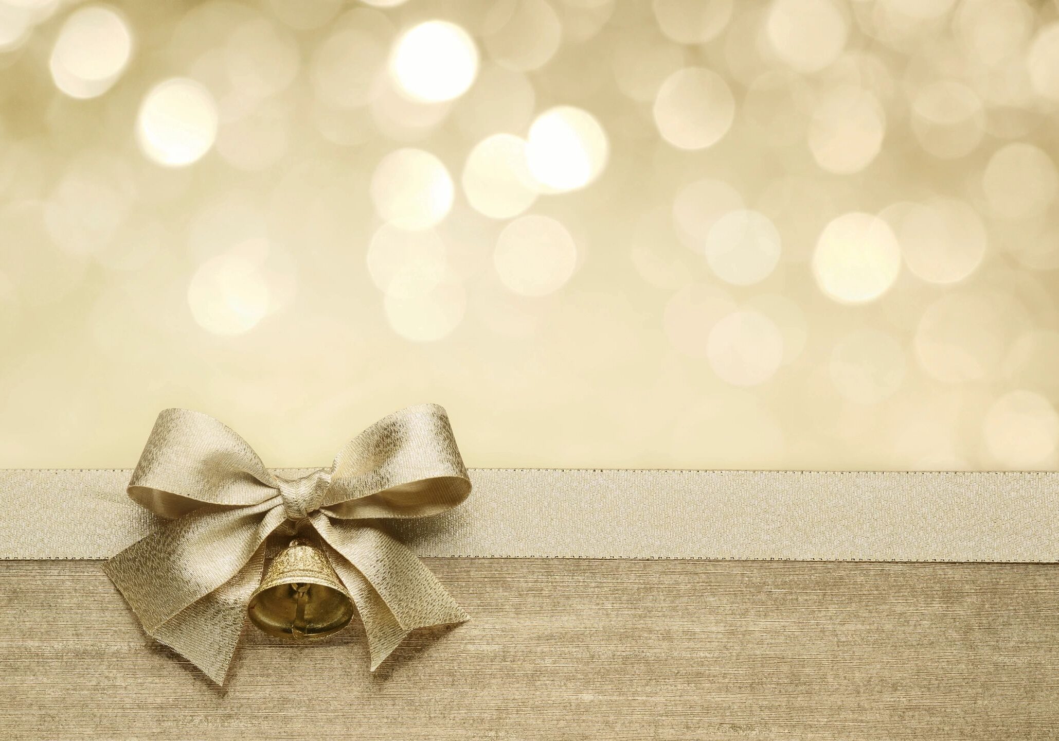 Elegant gold gift box with a bow on a wooden surface and bokeh lights.