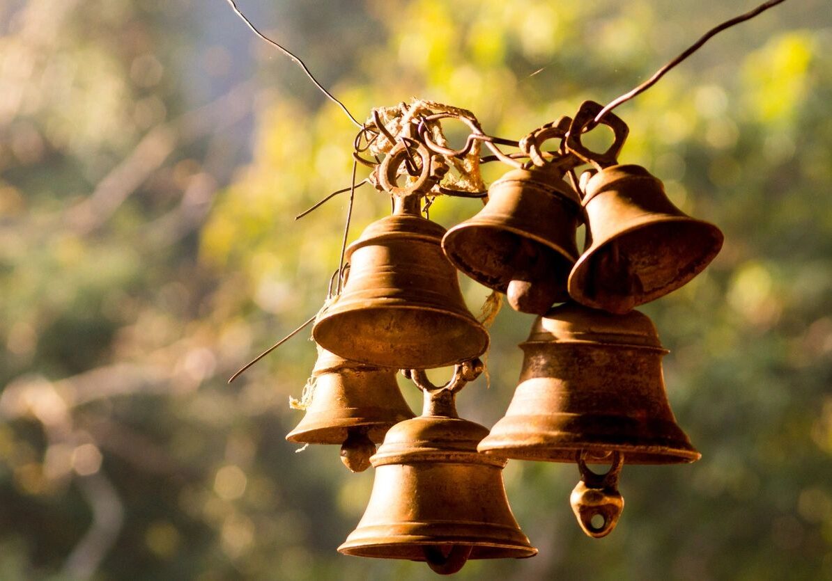 Rustic metal bells hanging outdoors with blurred natural background.