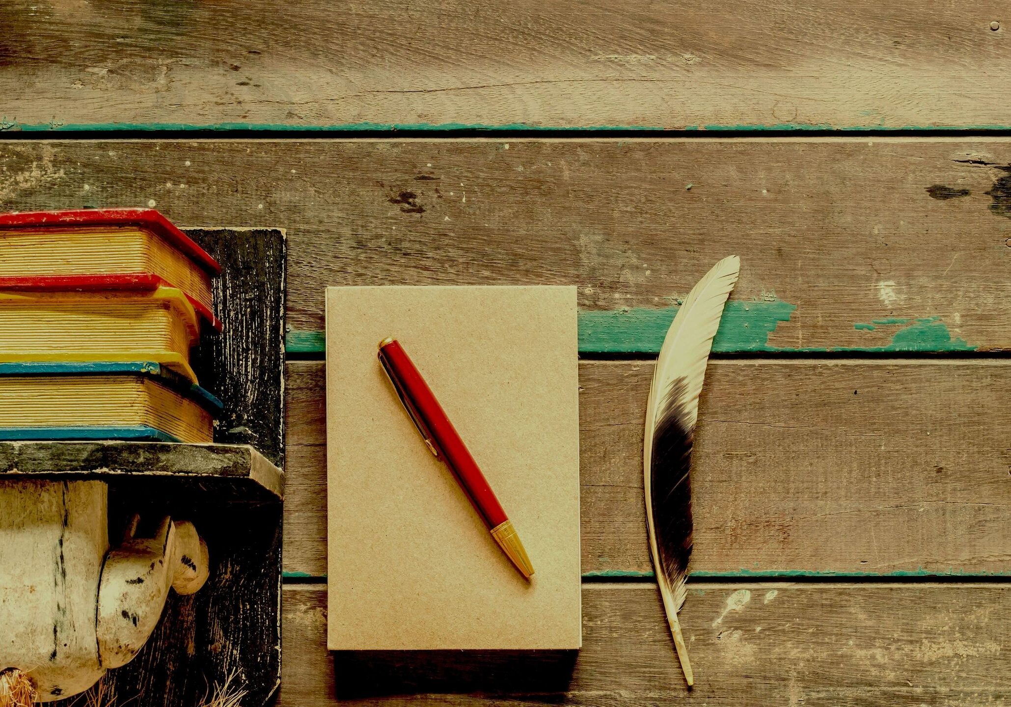 A notepad with a red pen and a feather on a wooden surface.