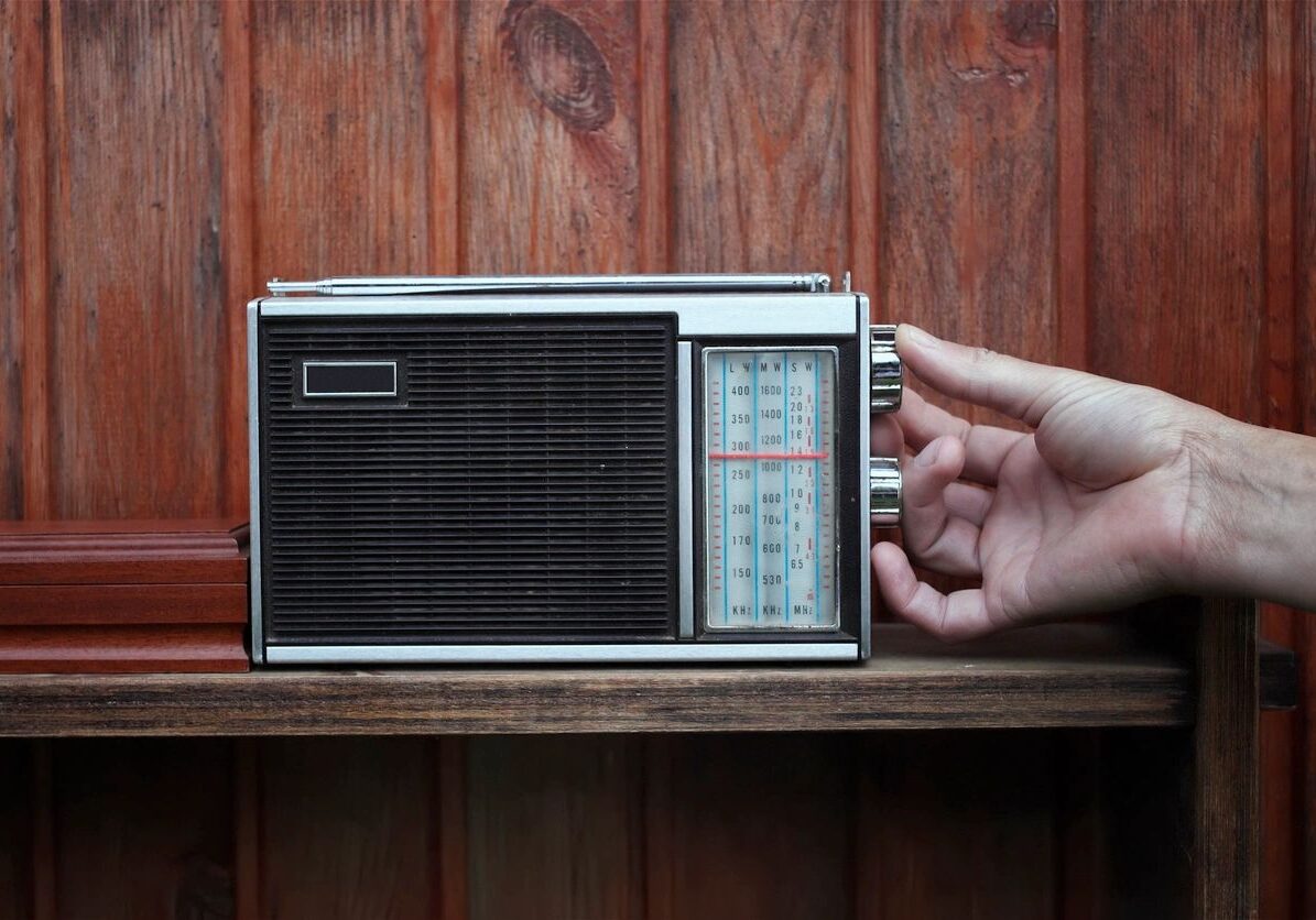 Hand tuning an old portable radio against a wooden background.