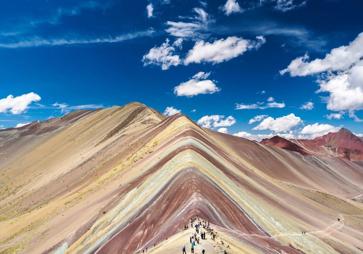 Rainbow Mountain's colorful striped slopes under a bright blue sky.
