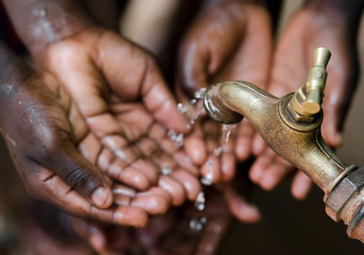 Hands catching water poured from a traditional vessel.