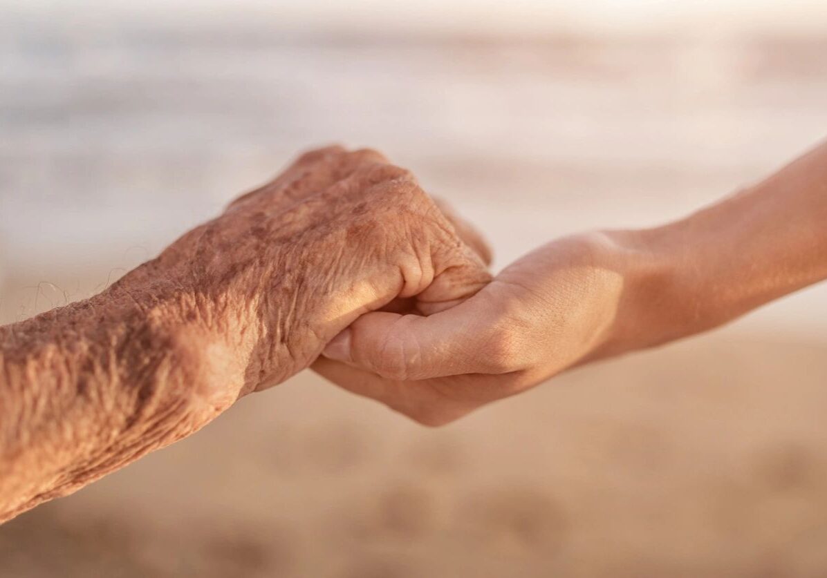An elderly hand holding a younger hand symbolizing care and connection.