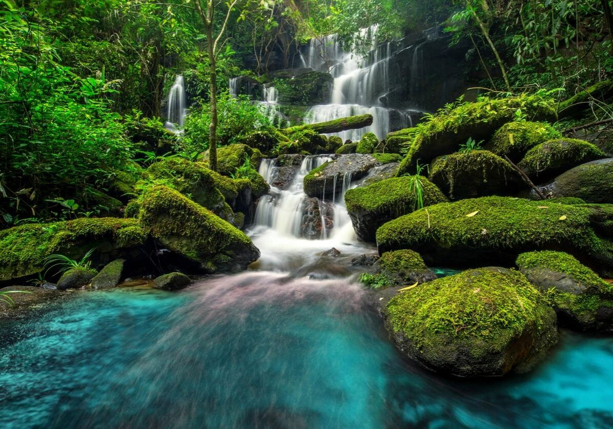 A serene waterfall flows over moss-covered rocks into clear blue water.