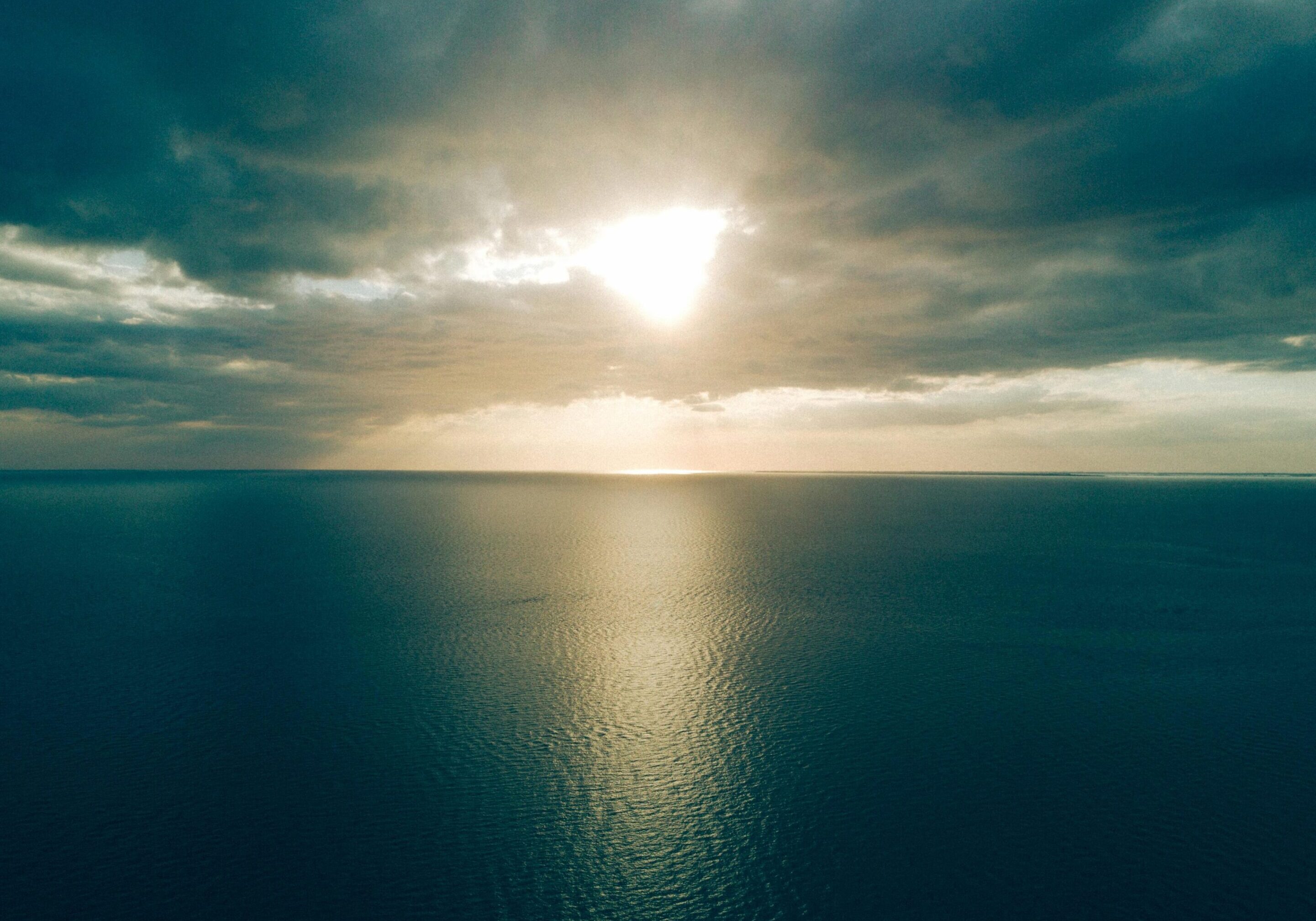 Sunlight piercing through dramatic clouds over a calm sea.