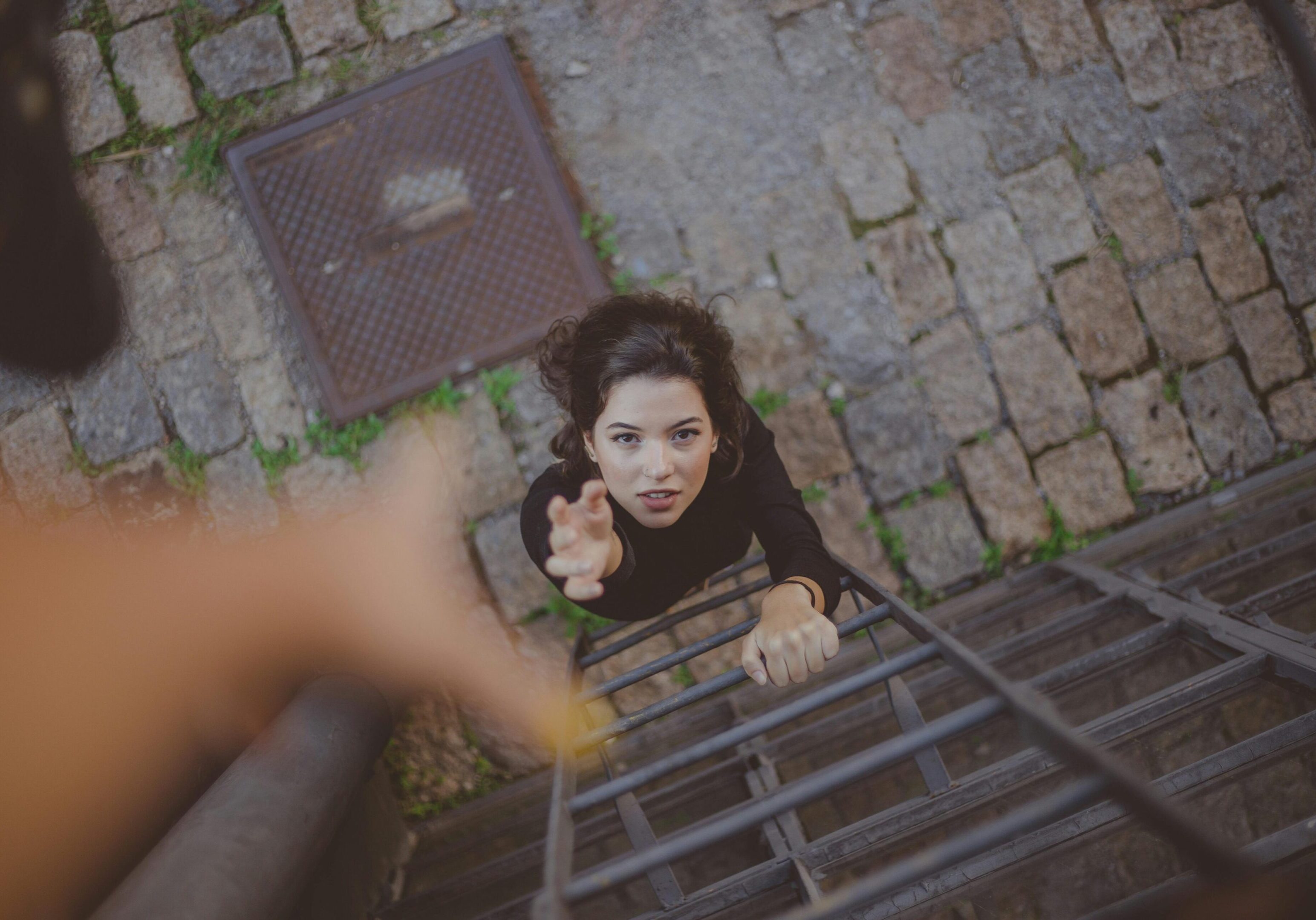 A woman reaches up a metal ladder with a hand extended toward her.