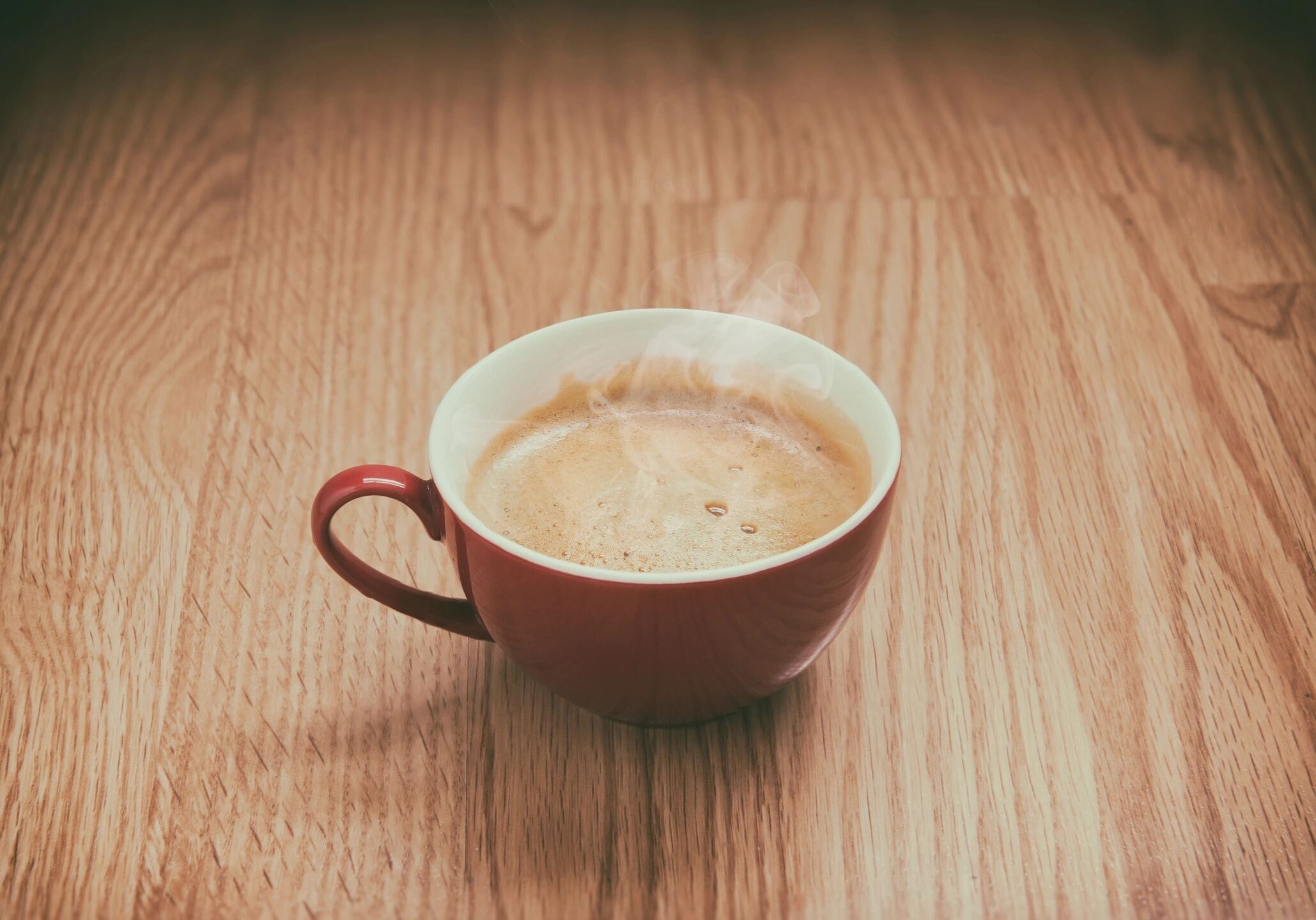 A cup of coffee with frothy foam on a wooden table.